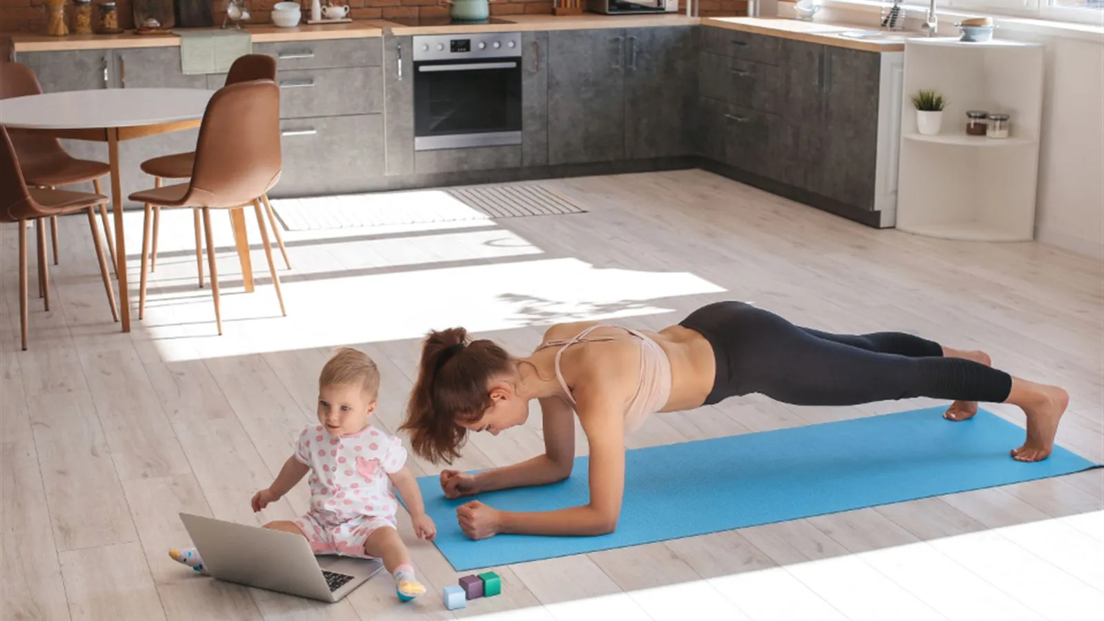 Mother doing a plank on a mat while a young child plays beside her